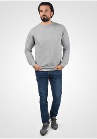 Gray pullover sweatshirt with a ribbed texture, round neckline, and long sleeves, paired with blue jeans and gray athletic shoes.