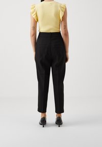 Zwarte, op maat gemaakte broek met een slim fit, voorzien van achterzakken, gecombineerd met een gele geribde top met ruches aan de mouwen.