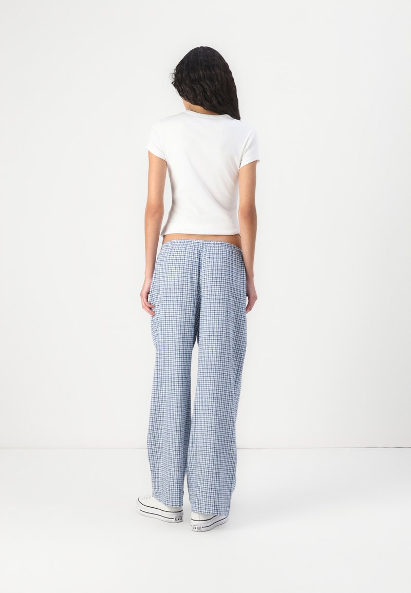 Szerokie, niebiesko-białe spodnie w krate o luźnym kroju, z elastycznym pasem. Połączone z dopasowanym białym t-shirtem i sneakersami.