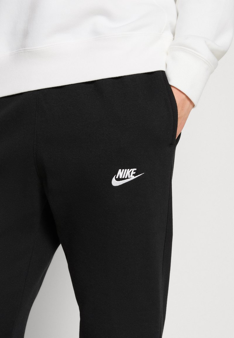 Pantalones de chándal negros de Nike con un logo blanco en el muslo, confeccionados con una tela suave, de corte relajado y con bolsillos.