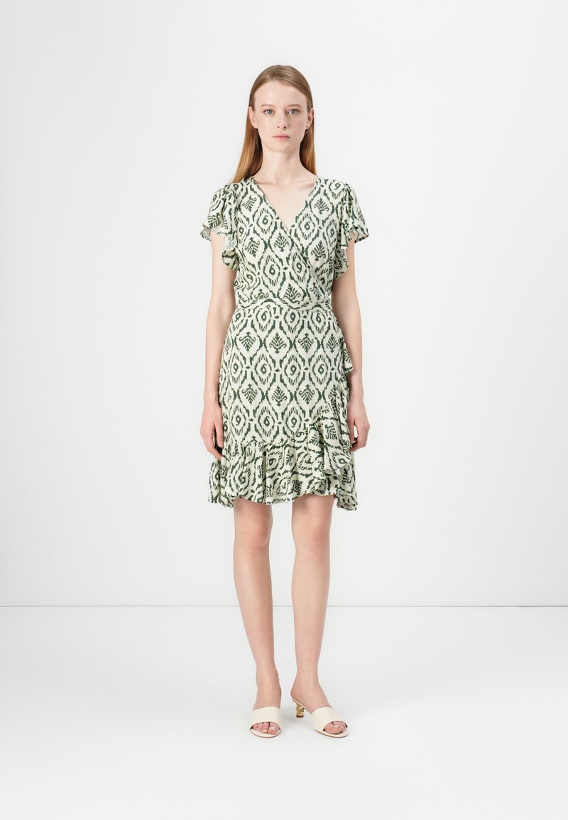 Απαλή πράσινη φόρεμα-τύλιγμα με λουλουδένιο μοτίβο, φουσκωτά μανίκια και στρωτό στρίφωμα. Συνδυασμένο με απλές μπεζ παντόφλες.