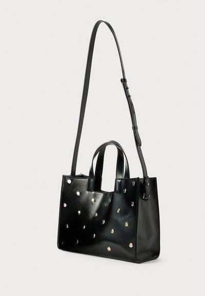 Sac fourre-tout en cuir noir avec deux poignées supérieures et une bandoulière réglable. Doté de clous en métal argenté disposés uniformément sur la surface.