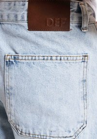 Lys blå denimjeans med en baklomme med kontrastsøm og et brunt lærmerke med prentet "DEF."