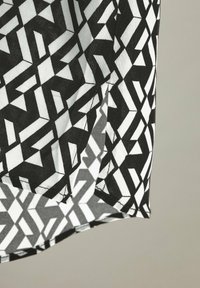Schwarz-weißes, geometrisch gemustertes Gewebe mit winkligen Formen und unterschiedlichen Texturen, das gefaltete Kanten und kontrastierende Farbsegmente aufweist.
