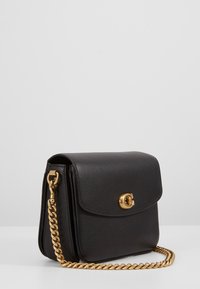 Borsa a tracolla nera in pelle con una tracolla in metallo color oro, chiusura a pattina con un fermaglio circolare e superficie testurizzata.
