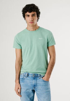 Mintgrønn bomull T-skjorte med rund hals og korte ermer, med en liten hvit logo på brystet. Brukt med lyseblå jeans.