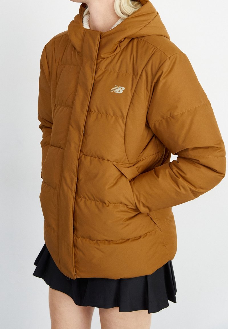 Brown puffer jacket with a hood, featuring quilted sections, a lightweight texture, and a small silver logo on the chest.