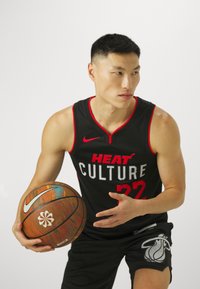 Black basketball jersey with red accents, "HEAT CULTURE" text, and number 22. Black shorts feature a Miami Heat logo. Player holds a multicolored basketball.