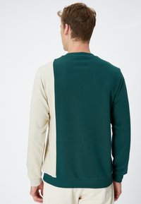 Sudadera verde y beige con un diseño de bloques de color. Presenta un cuello redondo y puños acanalados. Fabricada con un material suave y elástico.