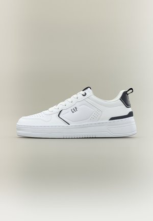 Witte lage sneaker met zwarte accenten, geperforeerde details, veters en het "GAP"-logo aan de zijkant, zijaanzicht tegen een neutrale achtergrond.