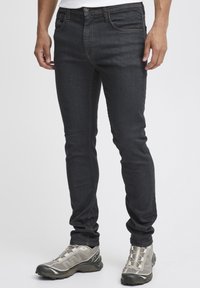 Mörka denimjeans har slim fit, kontrasterande sömmar och femficksdesign. Kombinerat med ljusgrå sportskor.