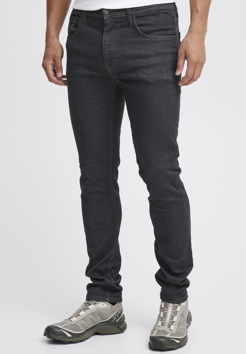 Mörka denimjeans har slim fit, kontrasterande sömmar och femficksdesign. Kombinerat med ljusgrå sportskor.