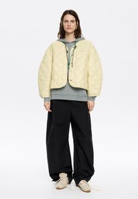 Lichtgele gewatteerde jas met een cropped ontwerp, gecombineerd met een grijze hoodie, zwarte wijde broek en beige sneakers.