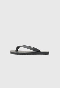 Svart flip-flop med teksturerte stropper, flat såle og taggete kant. Laget av gummi med en glatt overflate og minimalistisk design.