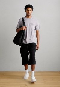 Γκρι βαμβακερό μπλουζάκι, μαύρο σορτς μέχρι το γόνατο, λευκά αθλητικά παπούτσια, κρατώντας μια μαύρη τσάντα ώμου. Απλός σχεδιασμός, απαλή υφή, χωρίς ορατά σχέδια.