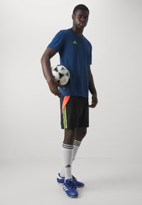Blue athletic shirt with green accents, black shorts with orange and yellow stripes, white socks, and blue soccer cleats. Holding a soccer ball.