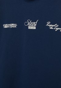 Tissu bleu marine avec trois motifs de texte blanc : "EPHEMERAL HERITAGE," "Stwd depuis 1991," et "Respectez l'héritage" dans différentes polices.