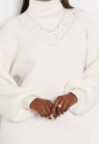 Maglione chunky bianco lavorato a maglia con colletto alto a dolce vita e un motivo a V con dettagli in pizzo sullo scollo; presenta maniche oversize e polsini a coste.