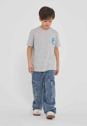 T-shirt in cotone grigio con maniche corte e grafica turchese sul petto, abbinata a pantaloni cargo in denim blu con tasche laterali.