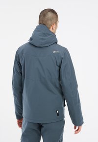 Donkerblauwe geïsoleerde jas met een capuchon, gemaakt van een lichtgewicht stof, met een logo op de bovenrug en elastische manchetten voor een goede pasvorm.