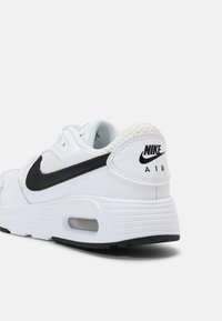 Bijela Nike Air tenisica s crnim Swoosh logotipom, gornjište od teksturirane kože, mrežasta podstava i vidljivo zračno jastučenje u potplatu.