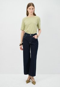 Camicia verde chiaro a maniche corte abbinata a pantaloni larghi in denim scuro a vita alta. I dettagli notevoli includono cuciture a contrasto e una chiusura con bottoni.