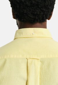 Lichtgele shirt gemaakt van textiel met structuur, featuring een button-down kraag, een centrale rugplooi en een enkele witte knop bij de kraag.