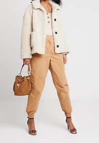 Veste en fausse fourrure crème, pantalon cargo marron avec poignets élastiques, sac à main marron avec quincaillerie dorée, et talons en imprimé léopard.