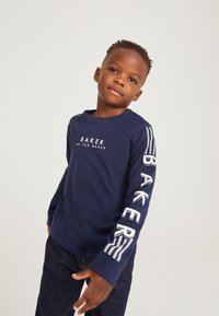 Marineblause mit langen Ärmeln und weißem "BAKER"-Logo auf der Vorderseite sowie fetter Schrift auf dem Ärmel. Kombiniert mit dunklen Jeans. Angenehme Textur, entspannter Schnitt.