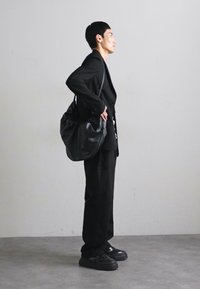 Juodas odinis peties krepšys su minkštu, užsilenkiančiu dizainu. Yra kreivės formos ir minimalus aparatūros naudojimas. Nešiojamas asmens, vilkinčio juodą pritaikytą kostiumą.