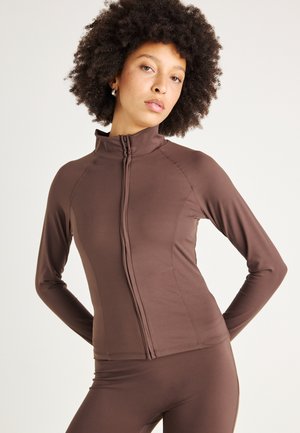 Brown long-sleeve zip-up jacket made of lightweight, stretchable fabric with a fitted design, featuring seam details along the body.