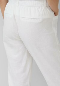 Pantalon en lin blanc à coupe décontractée, avec une taille élastique et deux poches arrière. Le tissu a une texture subtile.
