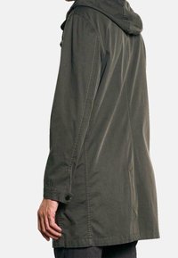 Oliwkowa, lekka kurtka z kapturem. Posiada długie rękawy, mankiety na guziki oraz prosty krój. Gładka tekstura, długość do kolan.