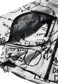 Biała kurtka z czarnymi wzorami graficznymi. Posiada kieszenie na zamek i teksturowaną podszewkę wewnętrzną. Wykonana z trwałego, lekkiego materiału.