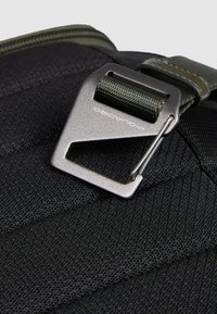 Tessuto nero con trama diagonale, caratterizzato da una fibbia grigio metallico e una cinghia verde, fissati con una clip argentata.