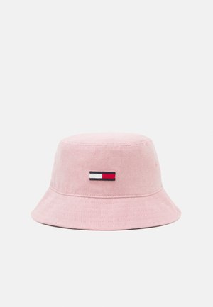 Chapeau bob rose clair avec un petit logo rectangulaire blanc, noir et rouge centré sur le devant.