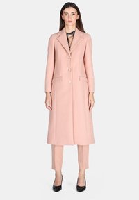 Cappotto lungo in misto lana rosa con vestibilità su misura, rever a taglio, tre bottoni e due tasche laterali, abbinato a pantaloni rosa coordinati.