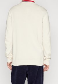 Cremefarbener Strickpullover mit hohem Kragen, der rote und marineblaue Streifen aufweist. Gerippte Bündchen und Saum, mit weicher Textur und legerer Passform.