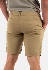 Pantalones cortos color caqui hechos de mezcla de algodón, con una textura suave, dos bolsillos traseros y dobladillo cosido. Sutil logotipo de la marca en la parte posterior.