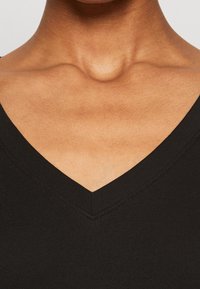 Svart V-ringad linne med ribbad textur och fint sydda kanter, som visar hudtonen vid halsringningen.