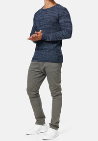 Suéter de punto azul marino con rayas texturizadas, cuello redondo, combinado con pantalones ajustados gris claro y zapatillas blancas.