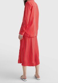 Rödrandig tvådelad outfit med en långärmad topp och en matchande kjol, båda med vertikala vita ränder, i ett lättviktsmaterial.