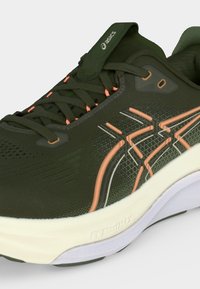 Σκούρο πράσινο αθλητικό παπούτσι Asics με ροδάκινο και λευκές λωρίδες, σκούρα πράσινα κορδόνια και λευκή μαξιλαρωμένη σόλα με το κείμενο "FF BlastMAX".