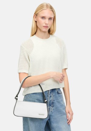 Sac à main blanc avec une bordure noire, de forme rectangulaire et avec une fine poignée. Porté par une personne portant un haut en tricot blanc texturé et un jean bleu.