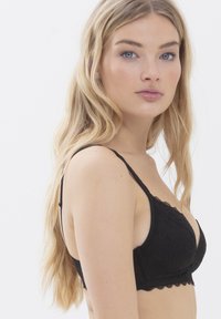 Zwarte kanten bralette met een golvende rand, dunne bandjes en een zacht driehoekig design. Beschikt over bloemmotieven en een gladde textuur.