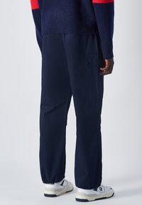 Marine Cargo-Hose mit lockerer Passform, ausgestattet mit seitlichen Taschen, elastischen Bündchen und kombiniert mit weißen Turnschuhen. Strukturierter Stoff sichtbar.