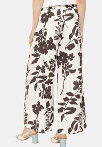 Pantaloni a gamba larga caratterizzati da un tessuto bianco con grandi stampe floreali marrone scuro. Vita elasticizzata, superficie liscia e vestibilità ampia.