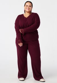 Ensemble de détente côtelé bourgogne comprenant un haut en V avec des poignets en dentelle et un pantalon ample, accentué par une coupe décontractée et une texture douce.