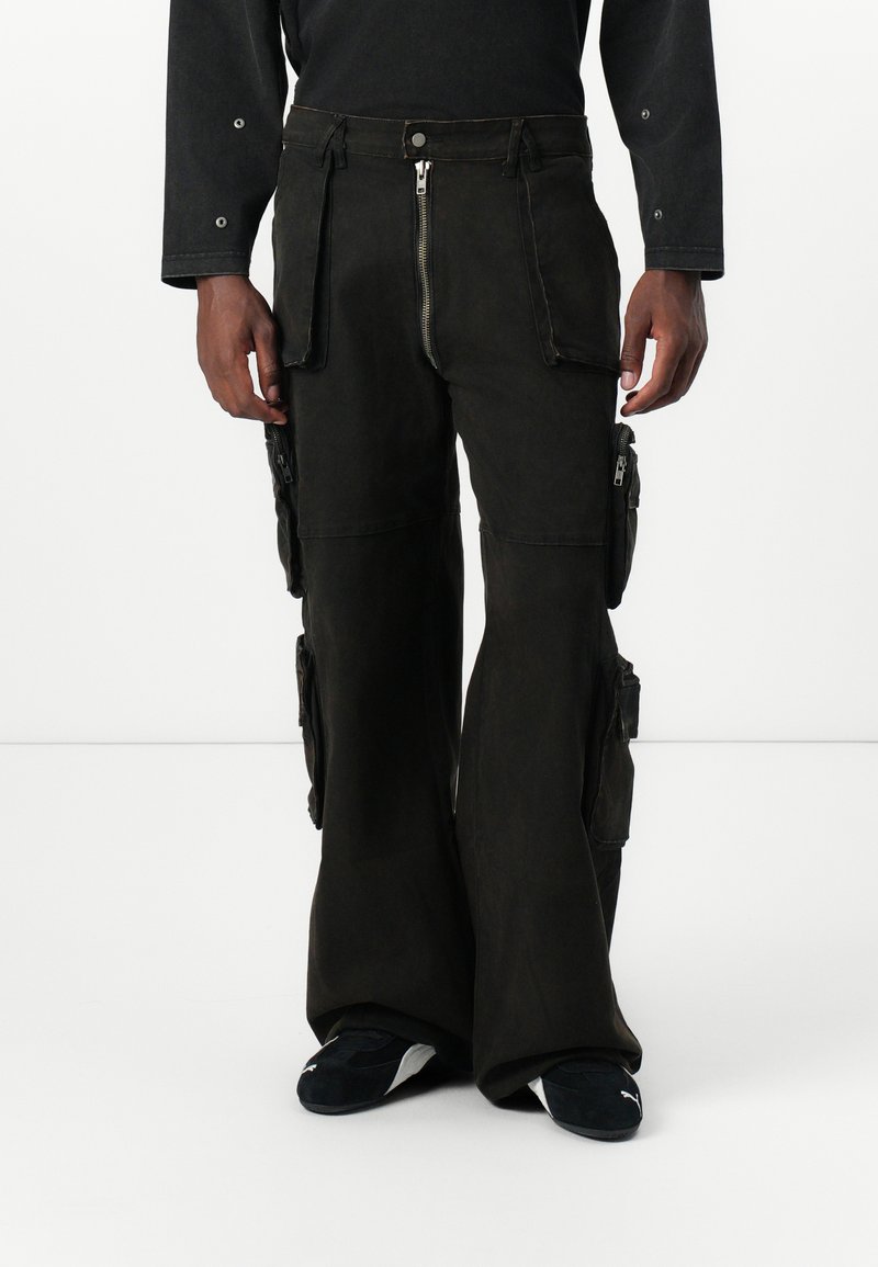 Donker cargo pants met een uitlopende vorm, meerdere zijzakken, ritssluitingen en een zachte, matte stoftextuur.
