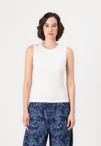 Haut sans manches blanc avec un col rond, fabriqué en tissu lisse, associé à un pantalon ample à motifs bleu foncé avec une taille élastique.